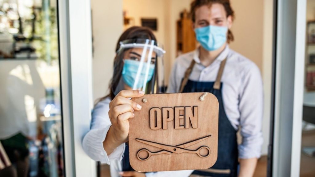 2 people with masks holding an open' sign for their hairdresser's business.